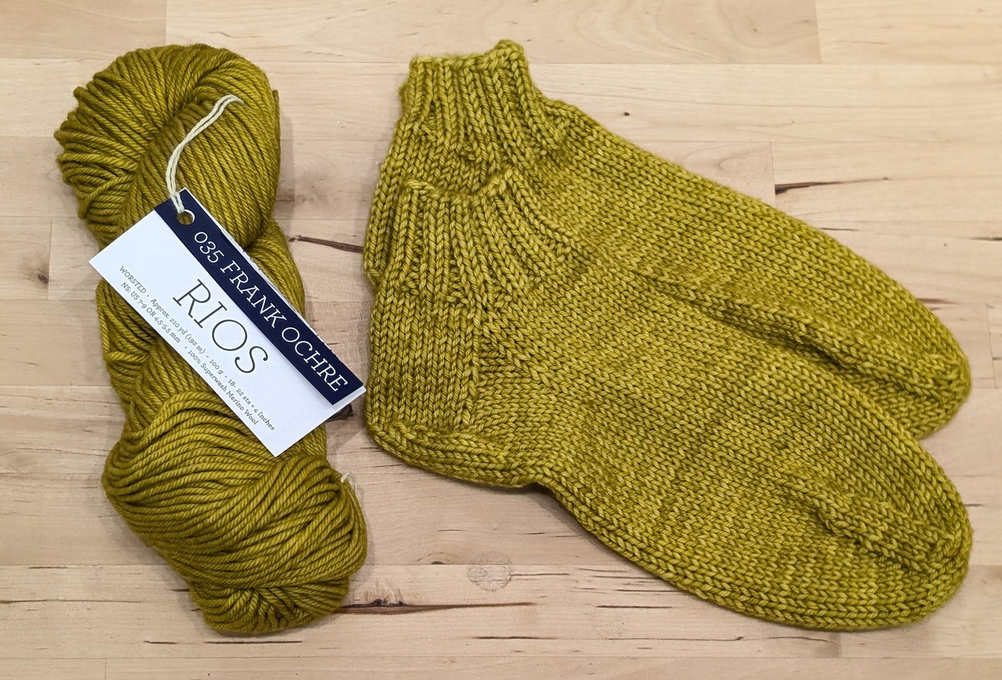 A pair of yellow knitted socks displayed next to a skein of Malabrigo Rios yarn.